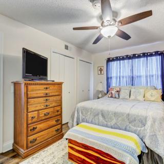 A cozy bedroom with a ceiling fan, dresser, TV, and a bed near a window with curtains.