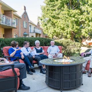 A group of people enjoying a conversation around a firepit on a patio in front of an apartment building.