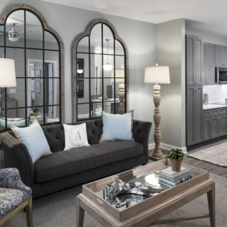 A stylish living room with gray tones, featuring a tufted sofa, decorative mirrors, and elegant lamps.