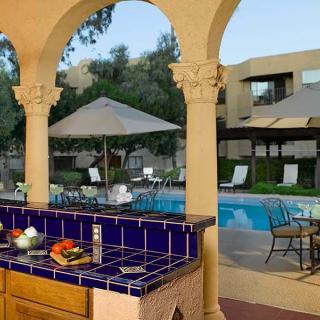 A serene poolside setting with tiled counters, patio furniture, and sun umbrellas.