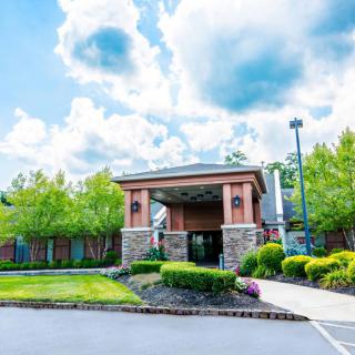 A welcoming entrance to a modern building surrounded by lush greenery under a cloudy sky.