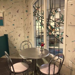 A cozy restaurant corner with a metal table, two chairs, and decorative stained glass windows.