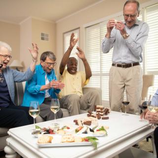 A group of joyful seniors celebrating together with snacks and wine indoors.
