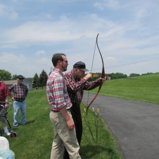 A group of people practicing archery outdoors on a sunny day.