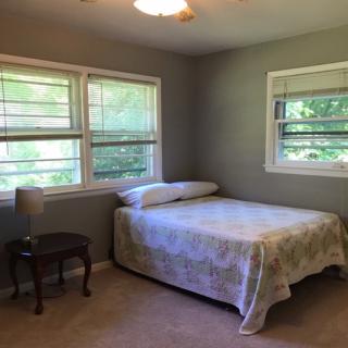 A minimalist bedroom with a bed, chair, and ample natural light from two windows.