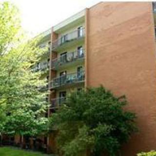 A brick apartment building with multiple balconies surrounded by trees.