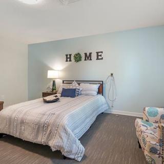 A cozy bedroom with a neatly made bed, soft lighting, and homey decorations on the wall.