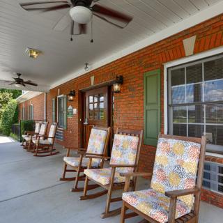A welcoming porch with rocking chairs and ceiling fans against a brick wall.