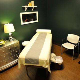 A cozy massage therapy room with a massage table, chair, and gentle lighting.