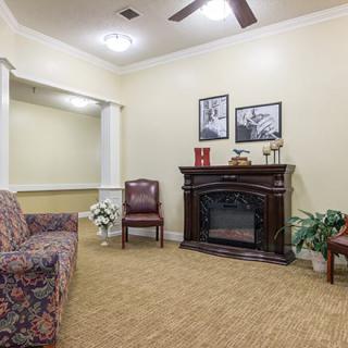 A cozy living room with a fireplace, sofa, armchair, and decorative plants.