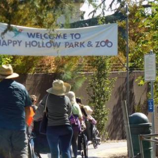 Visitors entering Happy Hollow Park & Zoo under a welcome banner.