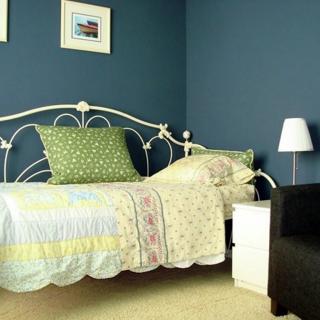 A cozy bedroom featuring a metal bed frame with colorful bedding, a nightstand with a lamp, and framed artwork on the wall.
