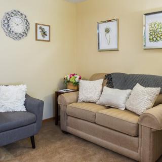 A cozy living room with a beige sofa and grey chair, adorned with decorative pillows and wall art.
