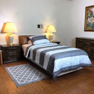 A cozy bedroom with a single bed, flanked by two nightstands and lamps, featuring a patterned rug and a dresser.