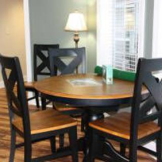 A cozy dining area with a round wooden table and chairs, softly lit by a standing lamp near the window.