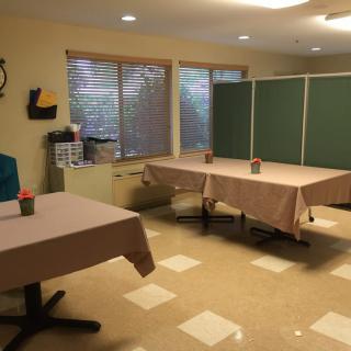A room with tables and chairs set up, featuring windows and wall decorations.