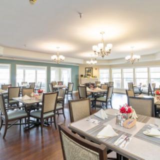 An elegant dining room with neatly arranged tables and chairs, illuminated by chandeliers.