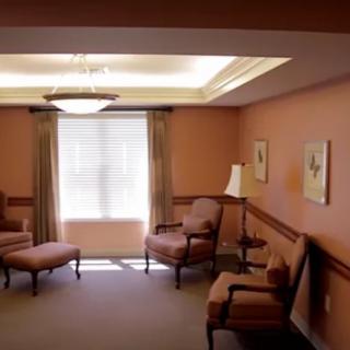 A cozy living room with upholstered chairs and a sofa, adorned with framed art and illuminated by soft lighting.