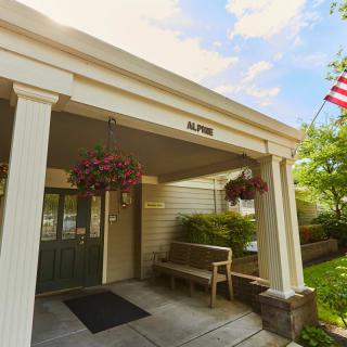 A building entrance with a covered walkway, displaying hanging flowers and an American flag.