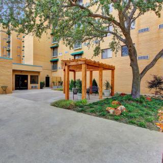 An apartment entrance with a walkway, surrounded by trees and landscaped garden.