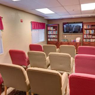 A small conference room with rows of chairs facing a television and bookshelves.