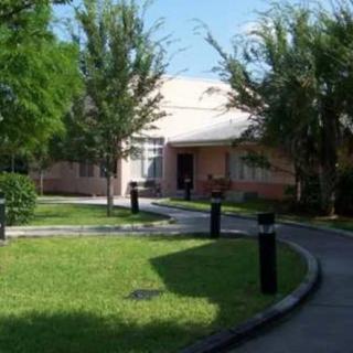 A house with a surrounding yard and pathway, flanked by trees and greenery under a clear sky.