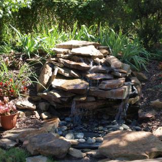 A serene garden water feature with cascading rocks surrounded by lush greenery.