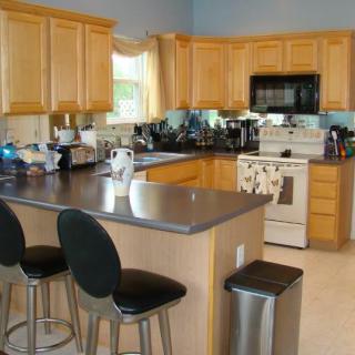 A modern kitchen featuring light wood cabinets, dark countertops, and stainless steel appliances with bar stools at the island.