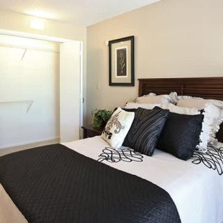 A modern bedroom with minimalist decor, featuring a neatly made bed with black and white accents and an open closet.