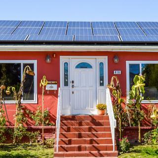 A charming red house with solar panels on the roof and a small front yard.