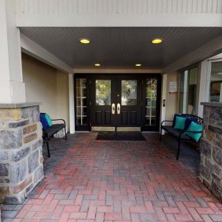 A covered entrance with double doors, brick walkway, and benches on either side.