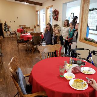 A group of children eagerly awaits their meal in a warmly decorated dining space.