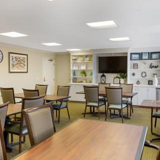 A well-lit dining area with neatly arranged tables and chairs, featuring a television and decorative shelves.