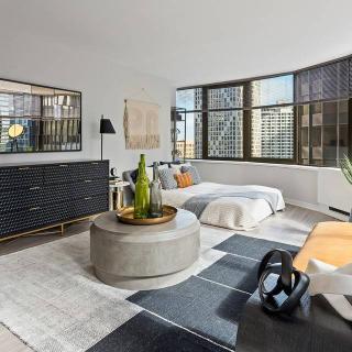A modern apartment with a spacious living room and bedroom area, featuring large windows offering a city view.
