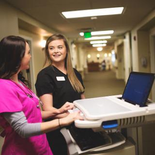 Two healthcare professionals engaging in a positive conversation while using medical technology in a hospital corridor.