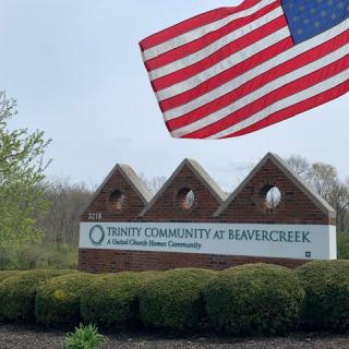 Sign for Trinity Community at Beavercreek with an American flag waving in the foreground.