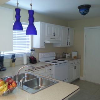 A modern kitchen with white cabinets and blue pendant lights over a countertop.