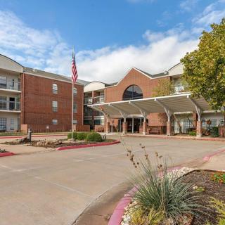 A residential building with a prominent entrance and landscaped driveway under a clear sky.