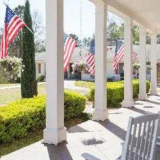 A sunlit patio with American flags displayed on the columns, overlooking a neatly trimmed garden.