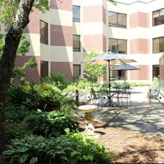 A peaceful courtyard featuring outdoor seating with tables, chairs, and umbrellas surrounded by lush greenery.