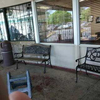 A view of an outdoor seating area with metal benches in front of a window.