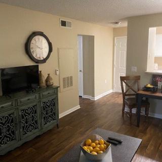 A cozy living room with decor and furniture, featuring a wall clock, television, and a table with chairs.