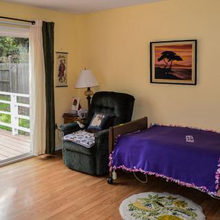 A cozy bedroom with a recliner, decorated with a purple blanket and a painting on the wall.