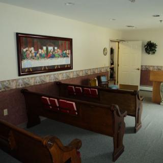 A small chapel interior with wooden pews and a religious painting on the wall.