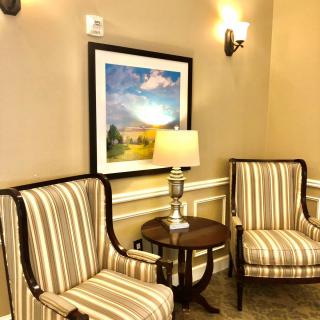 A cozy seating area featuring two striped chairs, a small table with a lamp, and a framed landscape painting on the wall.