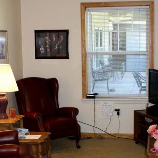 A cozy living room with armchairs, a lamp, a window, and a television.
