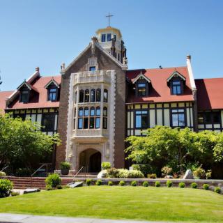 A historic university building with a manicured lawn and surrounding trees.