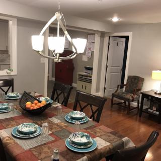 A well-set dining table in a cozy dining room featuring elegant dinnerware and a central fruit bowl under a modern chandelier.