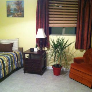 A cozy bedroom featuring a striped bedspread, a bedside lamp, and an orange chair.