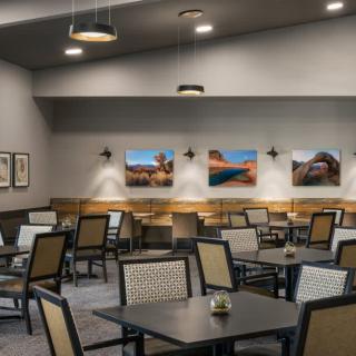 A modern restaurant interior with neatly arranged tables and chairs, complemented by artwork on the walls and soft overhead lighting.